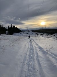 Person on snow covered field against sky during sunset