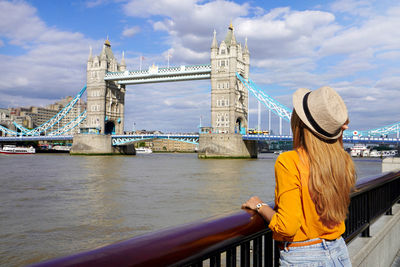 Girl leaning on the railing on river thames promenade with tower bridge famous landmark in london uk