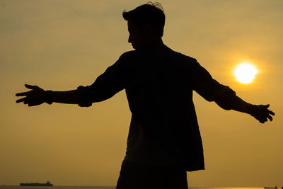 Rear view of silhouette man with arms outstretched standing against sky during sunset