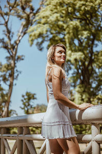 Portrait of beautiful young woman standing by railing on footbridge in forest