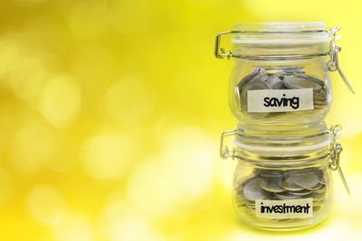 Close-up of coins in jar on yellow background