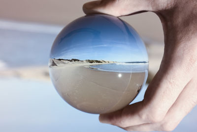 Close-up of human hand holding crystal ball with reflection at beach