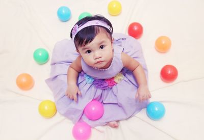 Directly above portrait of baby girl sitting amidst balls on bed at home