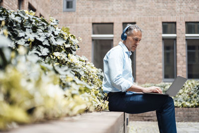 Businessman with headphones using laptop in office park