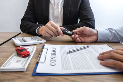 Agent giving car key to customer by papers and currency on table