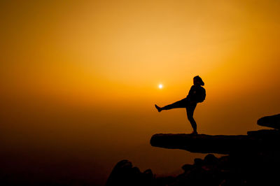 Silhouette woman kicking on cliff against sky during sunset
