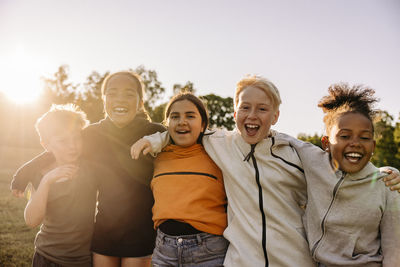 Portrait of cheerful kids with arms around playing together against sky