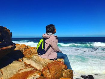 Woman sitting on rock by sea against clear sky