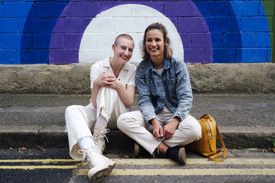 Happy young woman and non-binary person sitting on street