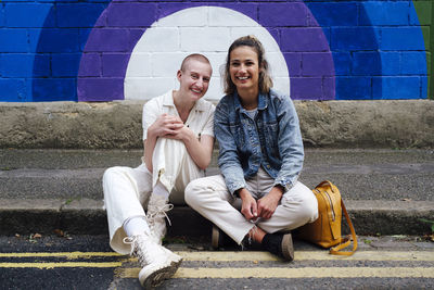 Happy young woman and non-binary person sitting on street