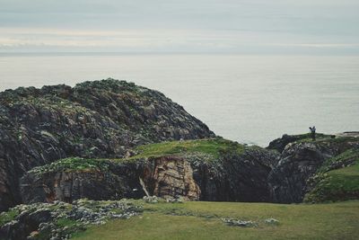 Man on rocky mountain by sea against sky