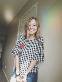 Portrait of smiling young woman standing against wall at home