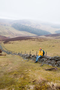 Full length of mid adult man sitting on retaining wall against sky