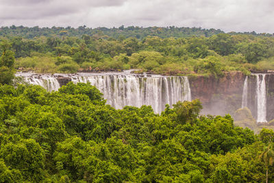 Scenic view of waterfall by trees against sky