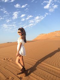 Side view of young woman standing on sand against sky