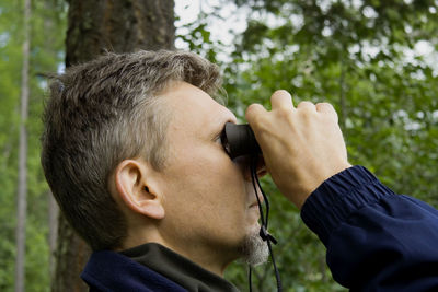 Side view of man looking through binoculars in forest