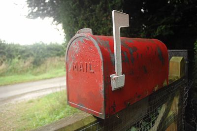 Close-up of old red mailbox on fence
