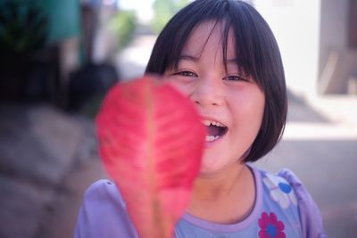 Portrait of smiling girl with red leaf outdoors