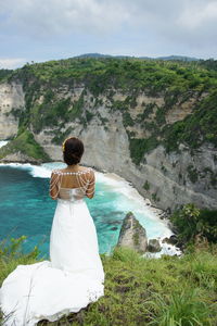 Rear view of woman standing on rock by sea