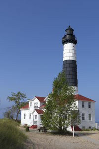 Low angle view of lighthouse by building against clear blue sky