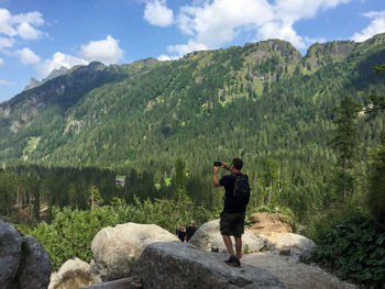Full length of man photographing on rock against sky