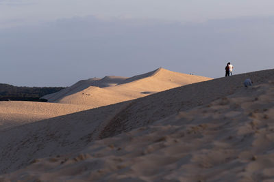 Rear view of man standing on sand dune in desert against sky