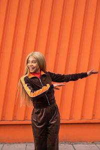 Cheerful african american woman in sportswear dancing in the street on an orange background