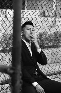 Young man looking away through chainlink fence