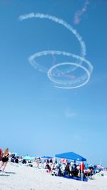 Tilt shot of people at beach during airshow in sky