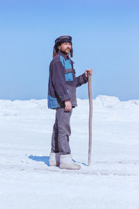 Mature man in ethnic clothes standing on mount of white sand or snow under blue sky. gypsum mining.