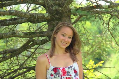 Portrait of smiling young woman standing against tree