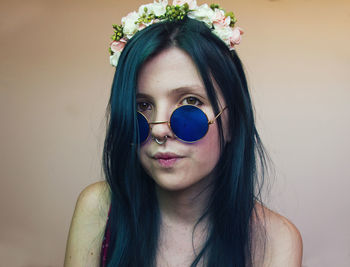 Portrait of woman wearing sunglasses while wearing flowers against wall