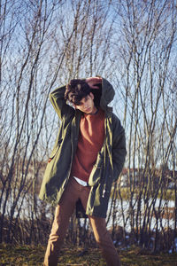 Young man wearing hooded jacket while standing against bare trees during winter
