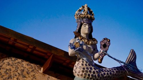 Low angle view of statue against blue sky and building