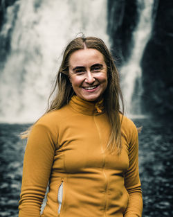 Portrait of young woman standing against waterfall
