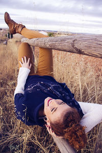 Happy young woman lying on railing at field