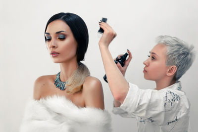 Beautician applying make-up to fashion model against white background