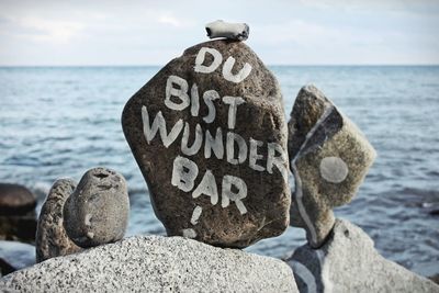 Text on rocks by sea against sky