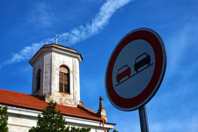 Low angle view of road sign by building against sky