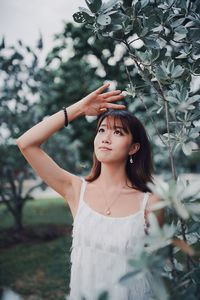 Beautiful young woman looking away while standing by plants