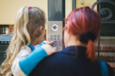 Close-up of mother carrying daughter typing password over security system on gate