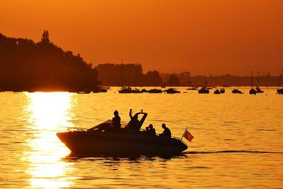 Silhouette people on boat in river against orange sky
