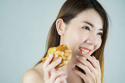 Portrait of a smiling young woman holding ice cream against gray background