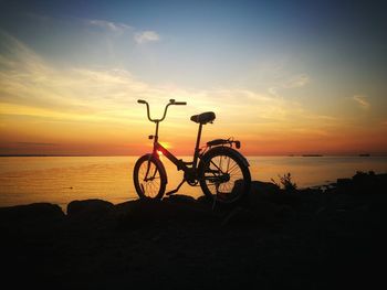 Bicycle by sea against sky during sunset