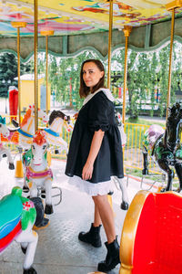 Beautiful brunette girl in a black dress poses on a bright carousel with horses