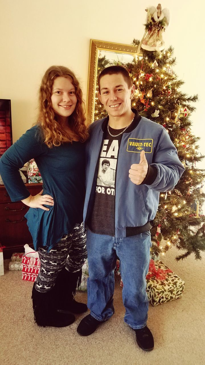 PORTRAIT OF HAPPY YOUNG COUPLE STANDING AGAINST TREE AT HOME