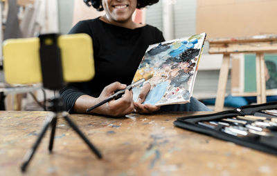 Young female artist showing paint palette while vlogging through smart phone at studio