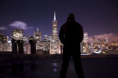Woman standing by illuminated cityscape at night