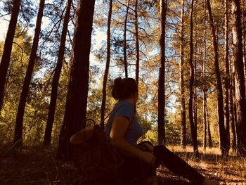 Side view of woman sitting on land against trees in forest