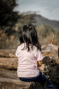 Rear view of young woman sitting on field